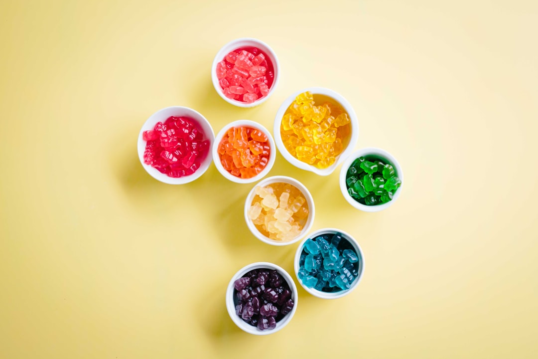 Colorful cannabis gummy edibles in white bowls arranged on a yellow background